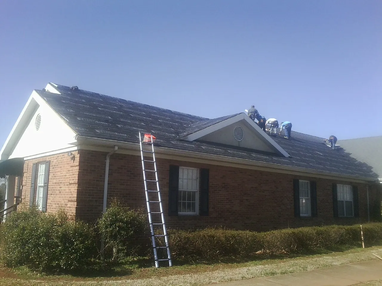 Crew tearing shingles off a brick ranch roof with a ladder set — Emergency Roof Repair work by our crew in Half Moon Bay