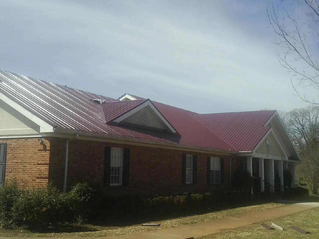 Red metal roof with gabled entries on a long brick building, from a Hail Damage Roof Repair job in Half Moon Bay
