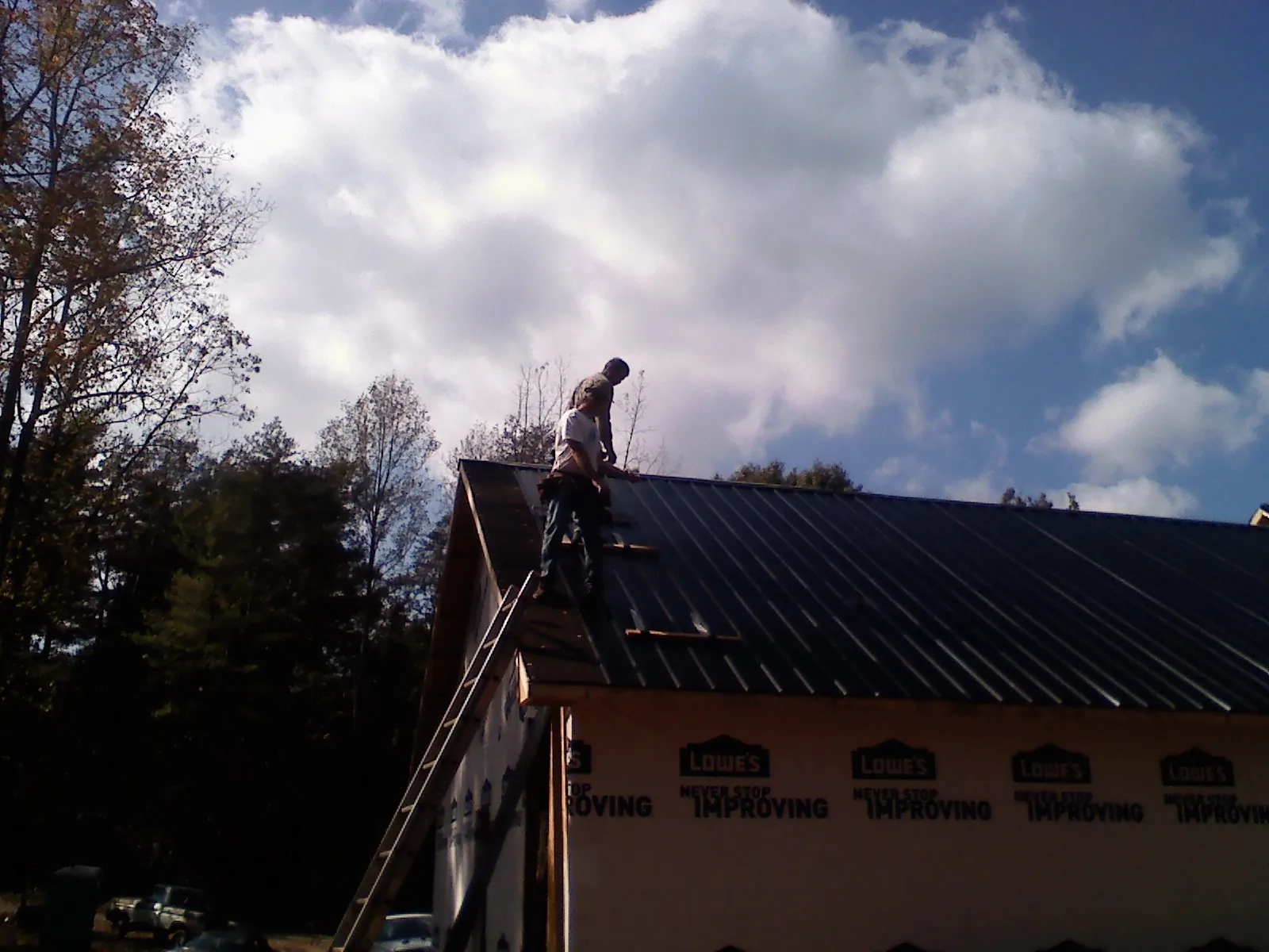 Roofer fastening dark metal panels high against a cloudy sky, from a Roof Inspection job in Half Moon Bay