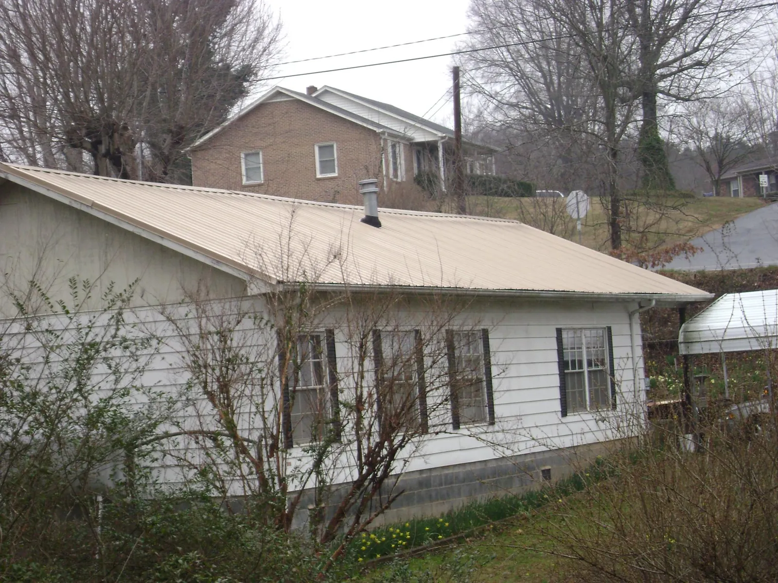 Tan metal roof on a white sided house set into a hillside — Commercial Roofing by Roofing Brothers in Half Moon Bay