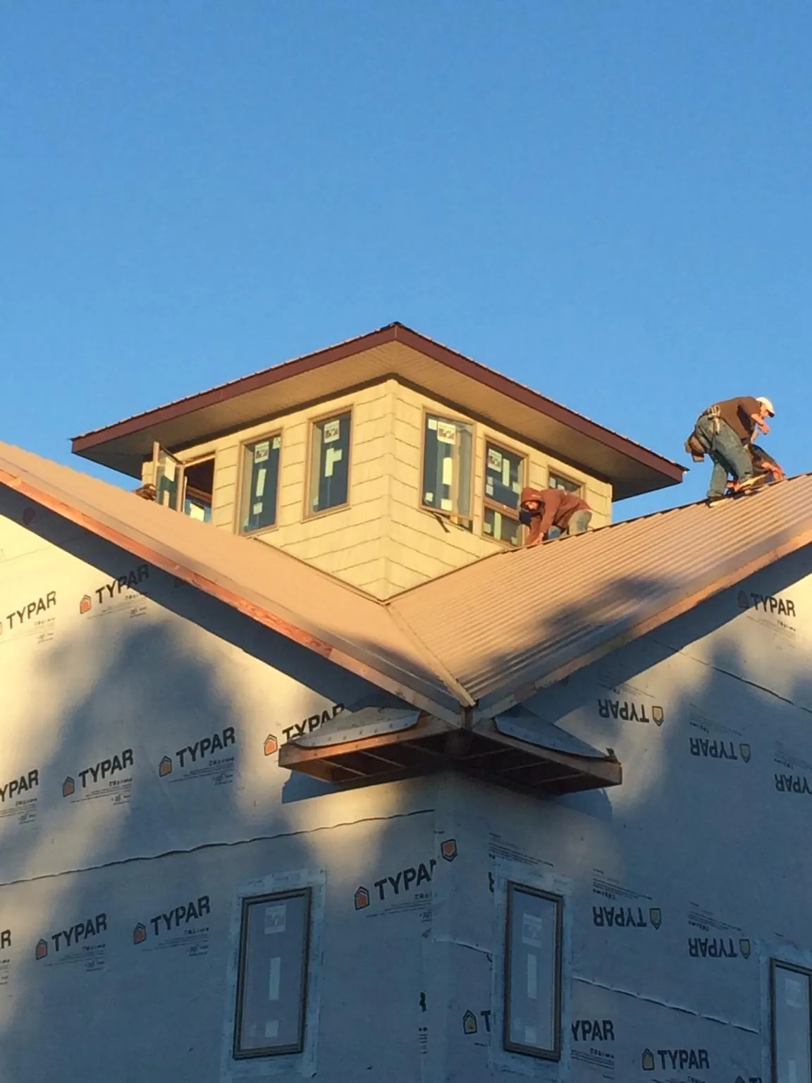 Roofers working around a rooftop cupola on a new metal roof at sunset in Half Moon Bay